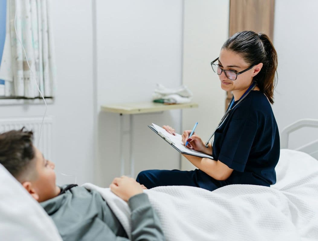 Pflegekraft notiert Informationen neben einem Patienten